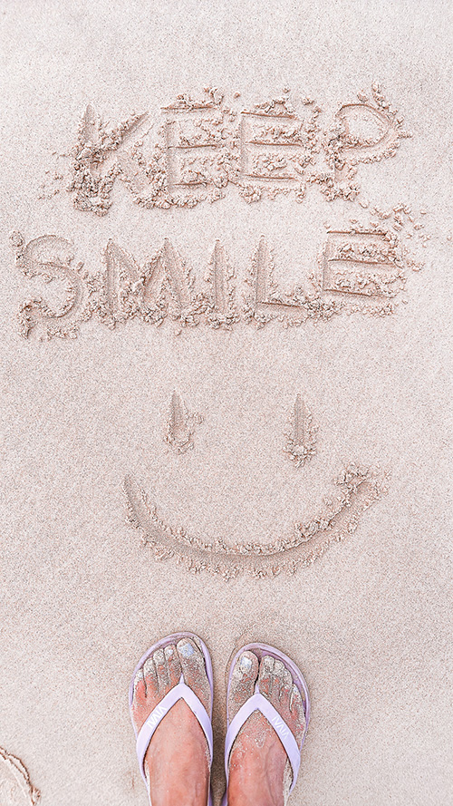完全無料の大人おしゃれな待ち受け・スマホ壁紙：砂浜に描いた「KEEP SMILE」の文字とスマイル