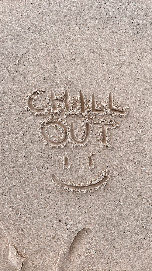 完全無料の大人おしゃれな待ち受け・スマホ壁紙：ビーチの砂の上に書いた「CHILL OUT」の文字とスマイル