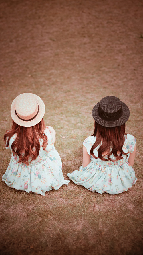 完全無料の大人おしゃれな待ち受け・スマホ壁紙：草原に座って景色を見ている双子の女の子たち