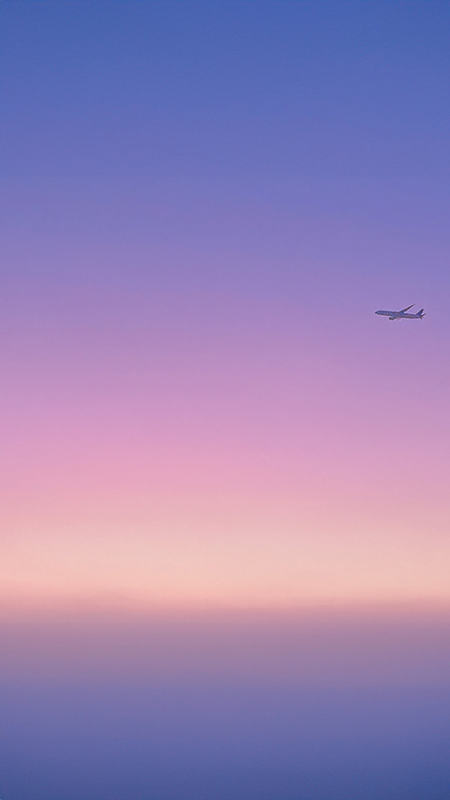 紫ピンクの夕焼け空を横断する飛行機