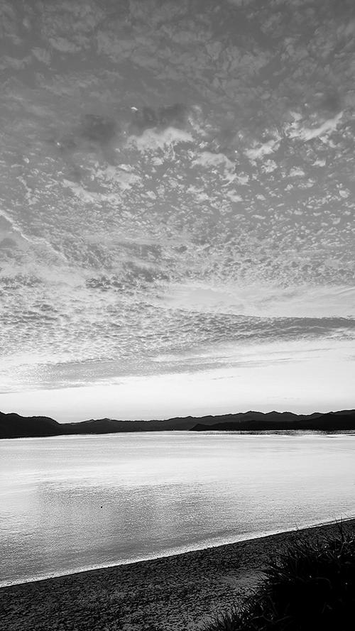 無料のおしゃれな縦長画像：穏やかな水面に映り込む夕焼けのグラデーションと美しい鱗雲（白黒版）