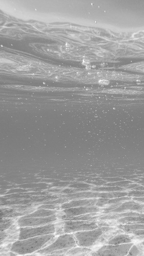 無料のおしゃれな縦長画像：太陽光が差し込む透き通った海中を立ち昇る気泡と水面の揺らぎ（白黒版）