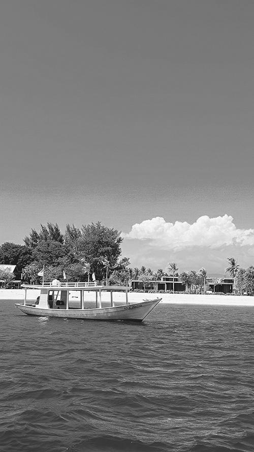 無料のおしゃれな縦長画像：美しい南国の白い砂浜と青い海に浮かぶ鮮やかなピンク色のボート（白黒版）