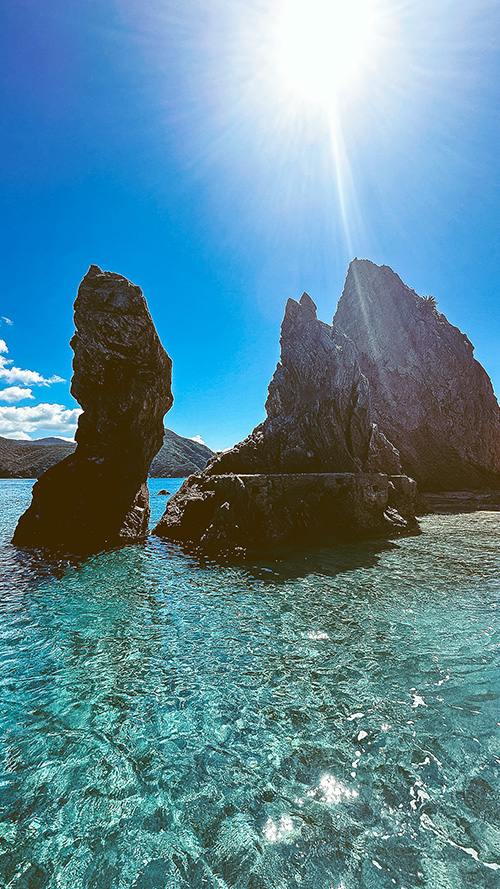 透き通るエメラルドグリーンの海にそびえ立つ岩肌と太陽の光